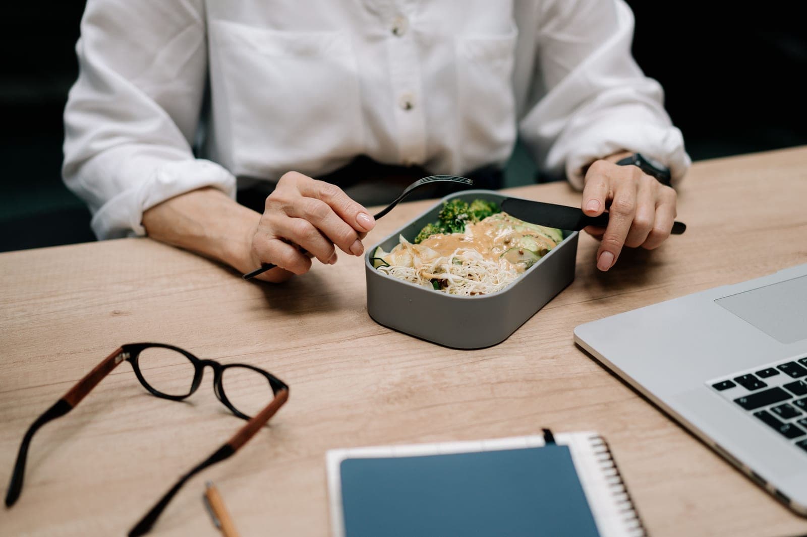 An adult eating a meal from a container at an office desk