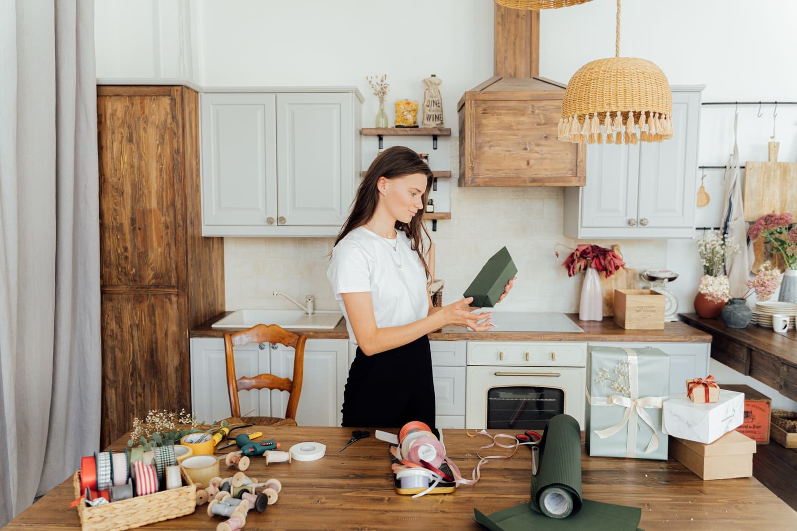 A woman wrapping a present with ribbon and paper in a kitchen