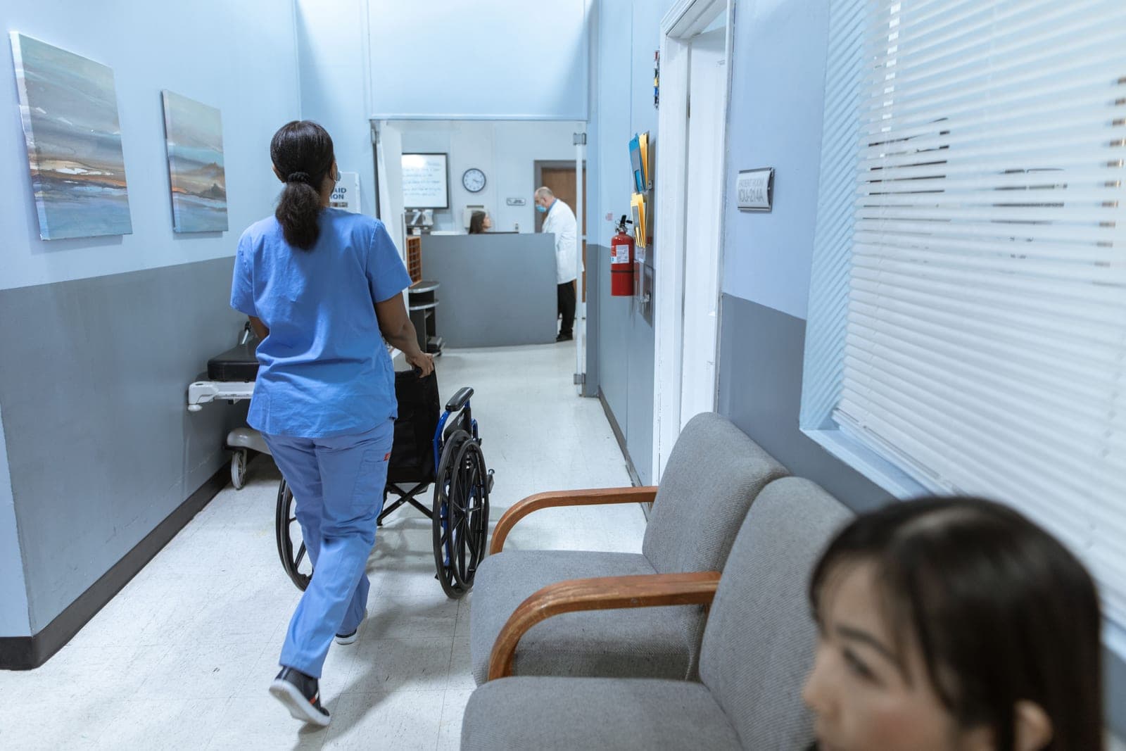 A nurse in scrubs pushing a wheelchair down a hospital corridor