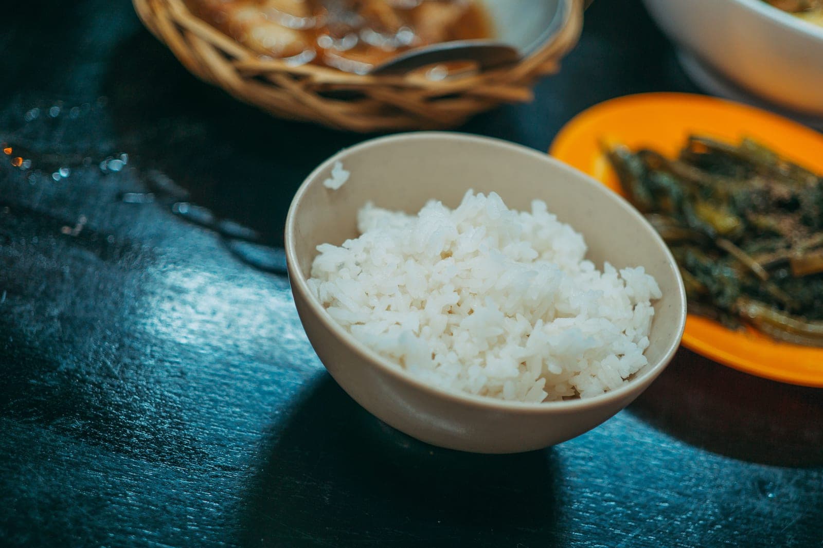 A bowl of white rice with sautéed vegetables beside it