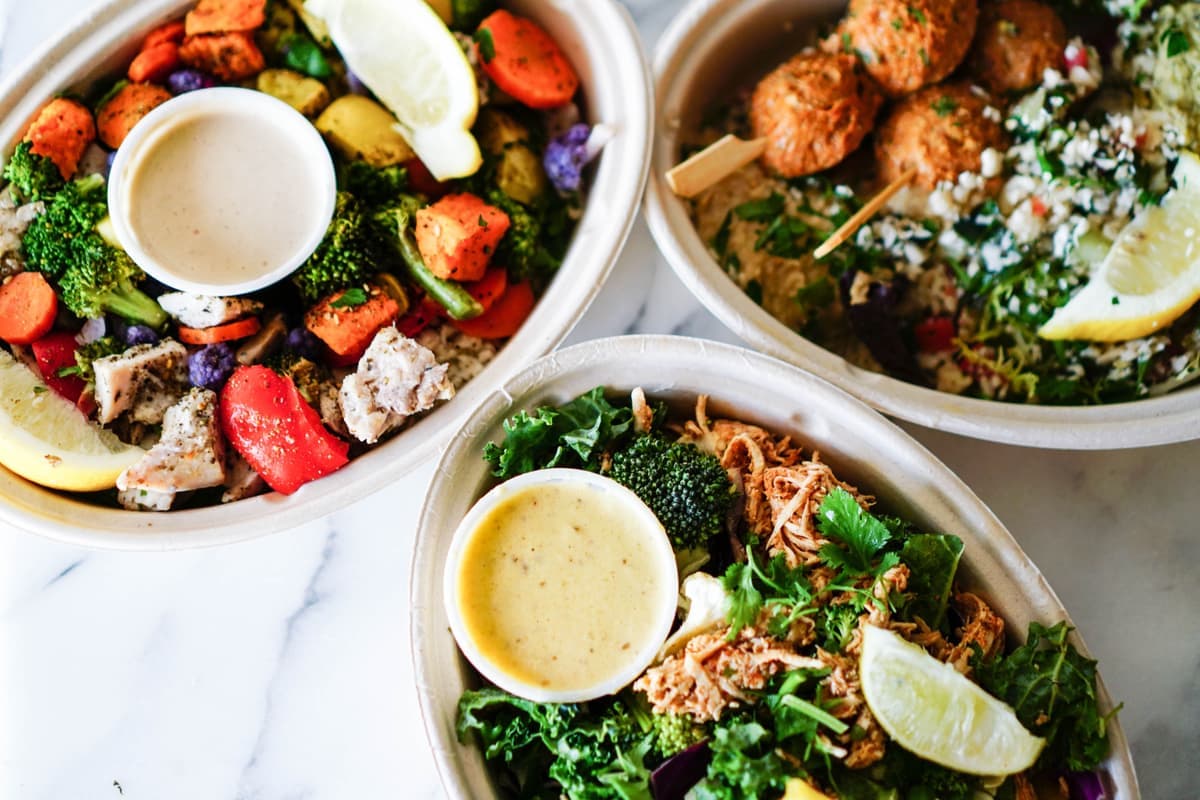 Meal bowls with roasted vegetables, salad and sauces, seen from above