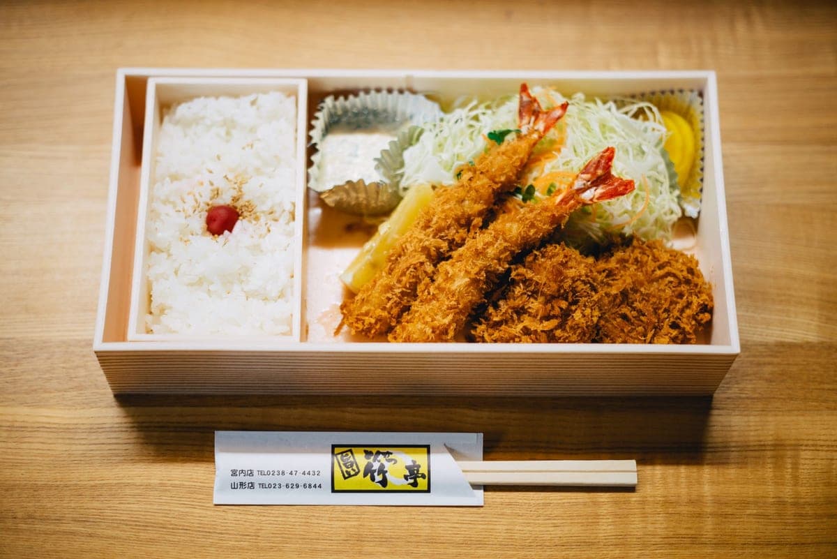 A bento box with rice, prawns and salad on a wooden table