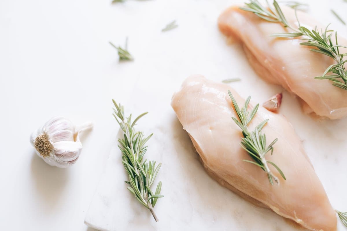 Raw chicken breasts with rosemary and garlic on a white surface