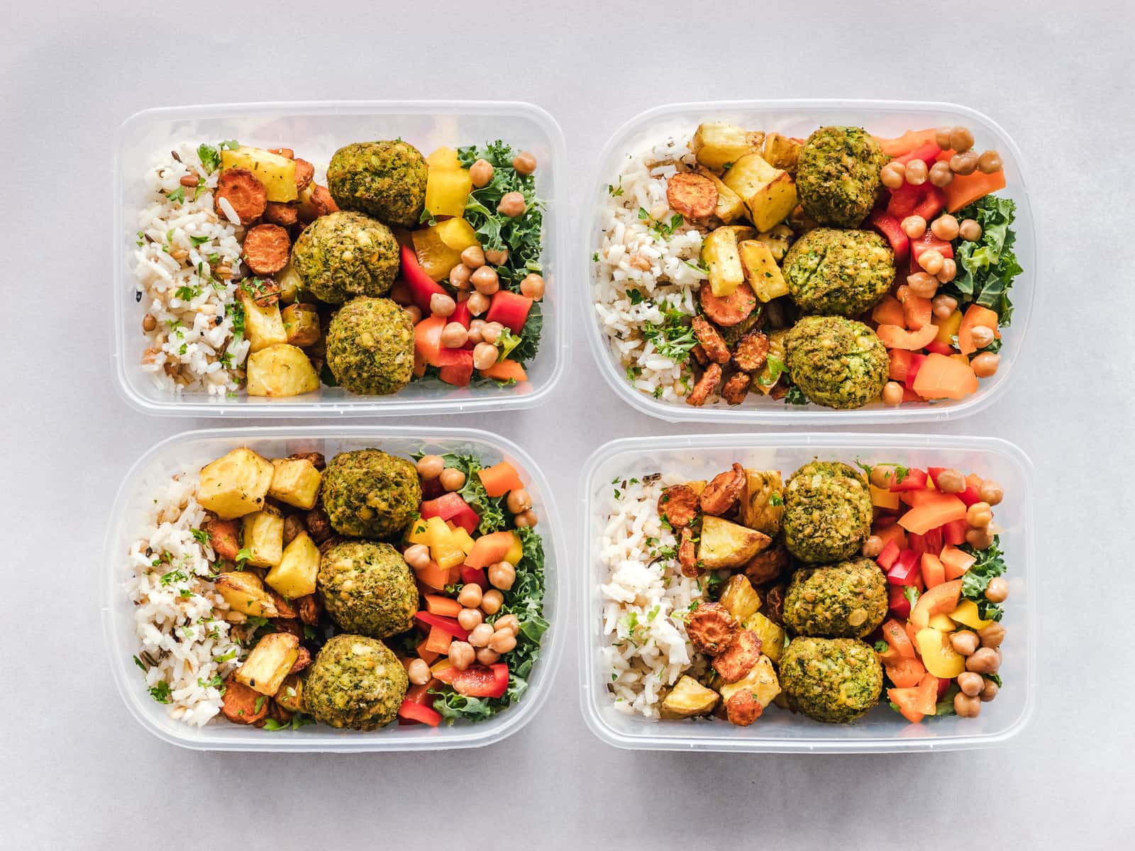 A row of meal prep containers with falafel, chickpeas, rice and vegetables